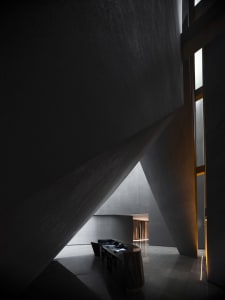 A minimalist hotel reception area with concrete walls and a sleek, black reception desk.