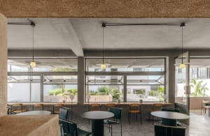 A modern industrial cafe interior with concrete floors and terrazzo countertops, large windows showcasing an outdoor greenery