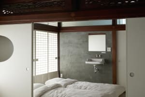 A small, minimalist bedroom with a concrete wall and white bedding.