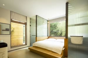A minimalist bedroom with a wooden platform bed, large windows, and natural light.