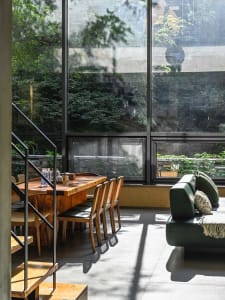 A minimalist living room with wooden furniture, large windows, and a green sofa.