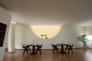 Minimalist restaurant interior with hardwood flooring, black tables, and white walls with a circular light fixture.