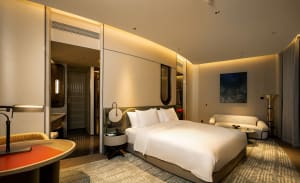 Modern bedroom suite featuring a textured white cloth headboard, plush white bedding, and a cozy seating area with a sofa and