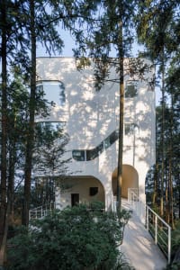 Modern, geometric architecture with concrete structure, situated in a forested area.