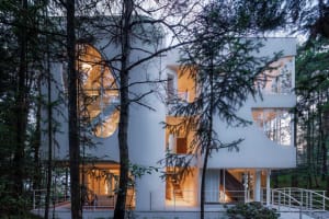 Modern residential building with large glass windows, white exterior, and stone base.