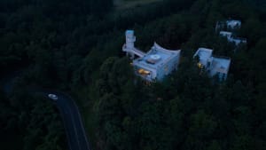 A modern residential building constructed of concrete with a curved roof and a winding road leading to it.