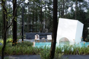 Modern residential exterior with a poolside relaxation space featuring wood, concrete, and glass materials.