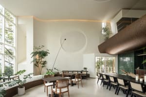 A modern restaurant interior with wooden furniture, white walls, and large windows.