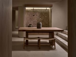 A minimalist dining room with a wooden table, chairs, and a vase of dried flowers.