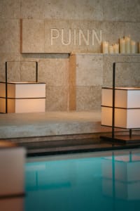 A minimalist spa setting with stone walls, lit candles, and a water feature.