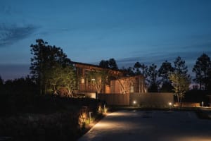 A modern building with wooden exterior and illuminated lights against a twilight sky.