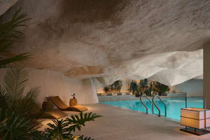 Luxurious spa pool cave with modern industrial design and white rock walls, illuminated by candles and sconces
