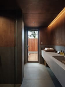 The image shows a minimalist bathroom featuring wooden walls and grey concrete flooring.
