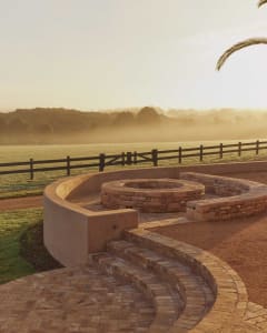 A landscape featuring a brick stone fire pit surrounded by a circular seating area.