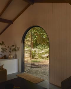 Interior view of a minimalist house featuring a wooden archway leading to a garden with greenery and plants.