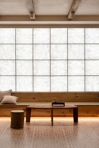 A minimalist living space featuring a large window with wood frames and a wooden table with a teapot and cup.