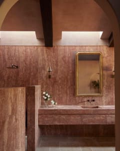 A modern bathroom featuring marble walls and a floating vanity with a golden-framed mirror and sleek fixtures.