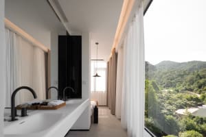 A minimalist bathroom with glass walls, concrete floor, and textile window treatments.