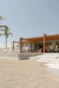 A beachfront resort with concrete and wooden structures, featuring a walkway and outdoor seating.