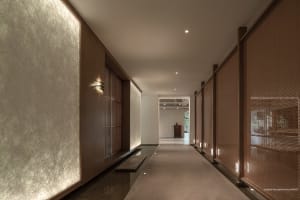 A minimalist corridor with wooden walls and paper screens, leading to a bright area with concrete flooring.
