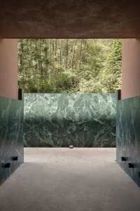 A minimalist, modern interior space featuring marble walls with a forest view.