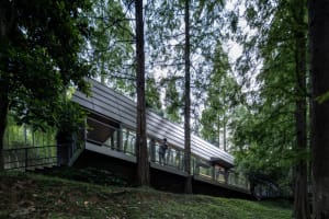 A modern house with metal-clad panels on the exterior, situated on a hillside surrounded by trees.