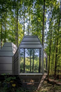 A modern modular house with metallic and glass elements in a forested setting.