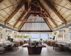 A spacious restaurant interior featuring wooden beams, open layout, and a view of the ocean.