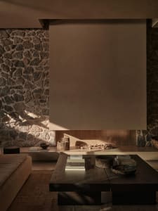 A modern living room with warm, earthy tones featuring a low wooden coffee table and a cozy stone fireplace.