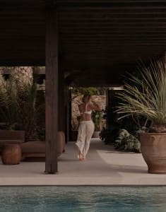 A minimalist outdoor space with concrete flooring, wooden columns, and tropical plants.