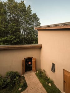 A modern exterior concrete garden with a fireplace and greenery surrounded by lush trees.