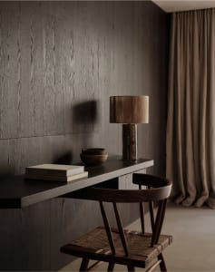 A modern home office desk with a wooden chair, lamp, and a few books.