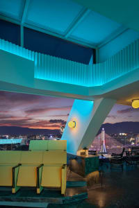 A modern concrete rooftop bar with vibrant lighting and a stunning city view.