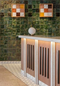 A modern commercial reception area featuring sleek wooden cabinets with black handles, a white countertop, and green ceramic 