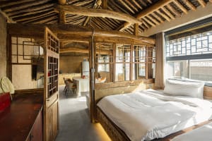A modern industrial bedroom featuring a wooden bed frame, natural wood ceiling beams, and a white bed with a wooden headboard