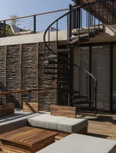 An industrial-style balcony featuring black metal stairs, wooden seating, and a wicker wall