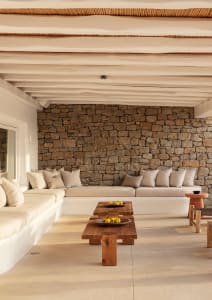 A minimalist living room featuring a natural stone wall and white furniture with accent pillows.