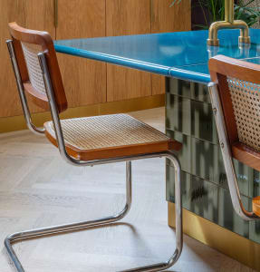 A modern kitchen design featuring a blue concrete countertop with metal legs, a wooden chair with woven chair back and seat, 