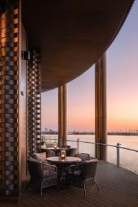 Outdoor patio area with wooden furniture surrounded by a wooden deck during sunset.