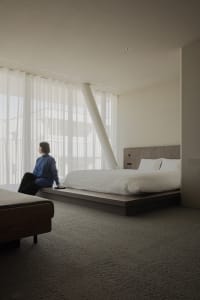 A serene minimalist bedroom with a white bed, grey carpet, and a wooden headboard.