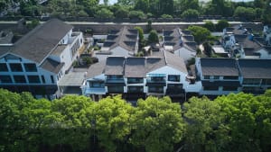 Aerial view of a traditional white village with gray-tiled roofs and green leafy trees.