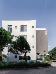 A modern building with a white rendered exterior and green trees in the foreground.