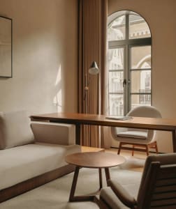 A cozy beige living room with a wooden table, white chairs, and a window overlooking a cityscape.