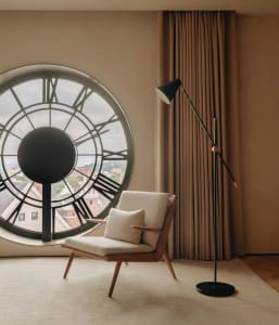 A minimalist living room featuring a modern chair, a floor lamp, and a circular window with a view of a cityscape.