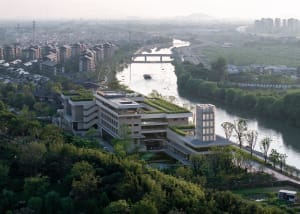 A modern office building with a concrete exterior and a landscaped riverfront.