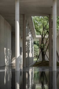 Concrete columns in a modern office setting, with a court area surrounded by greenery.