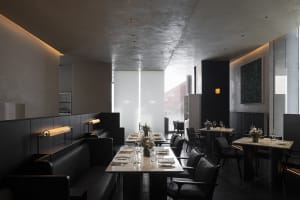 A modern restaurant with concrete walls and benches, featuring sleek furniture and minimalist decor.