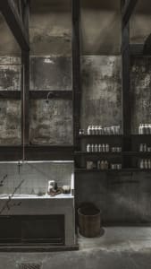 A modern, industrial-style bathroom with concrete walls and exposed beams, featuring a shower head mounted on the wall and va