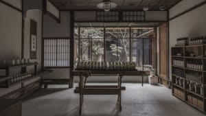 A traditional retail storefront with a wooden bench and bottles lined up on a table, viewed through a window with white paper