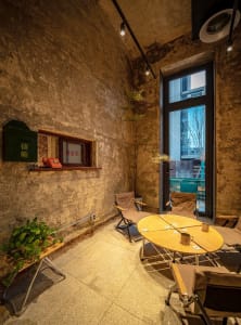 Industrial-style co-working space with concrete walls, wooden table and chairs, and a large window overlooking an urban lands